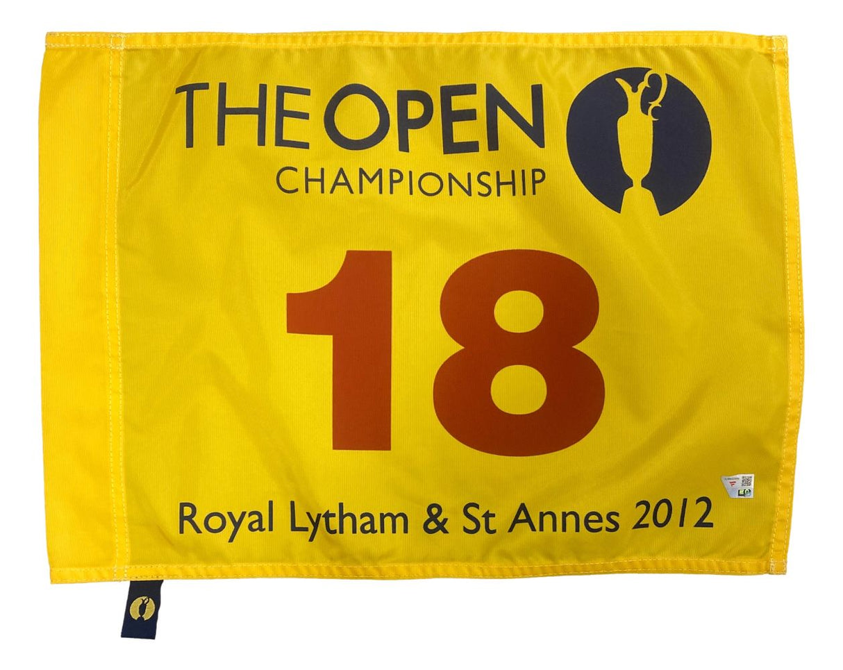 The 2012 Open Championship PGA Issued Golf Flag by Sports Integrity features a yellow design with THE OPEN CHAMPIONSHIP, a golf trophy logo, the red number 18, and "Royal Lytham & St Annes 2012" at the bottom.
