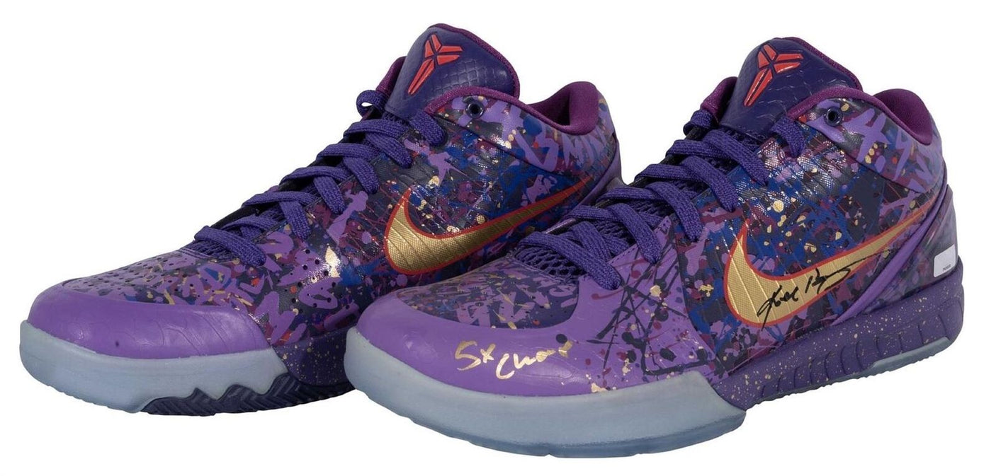 A pair of Sports Integrity Kobe Bryant Lakers Signed Nike Zoom Kobe IV Prelude Shoes with purple and gold accents, vibrant paint splatter, purple laces, Kobe logos on the tongues, and both autographed in black and gold marker.