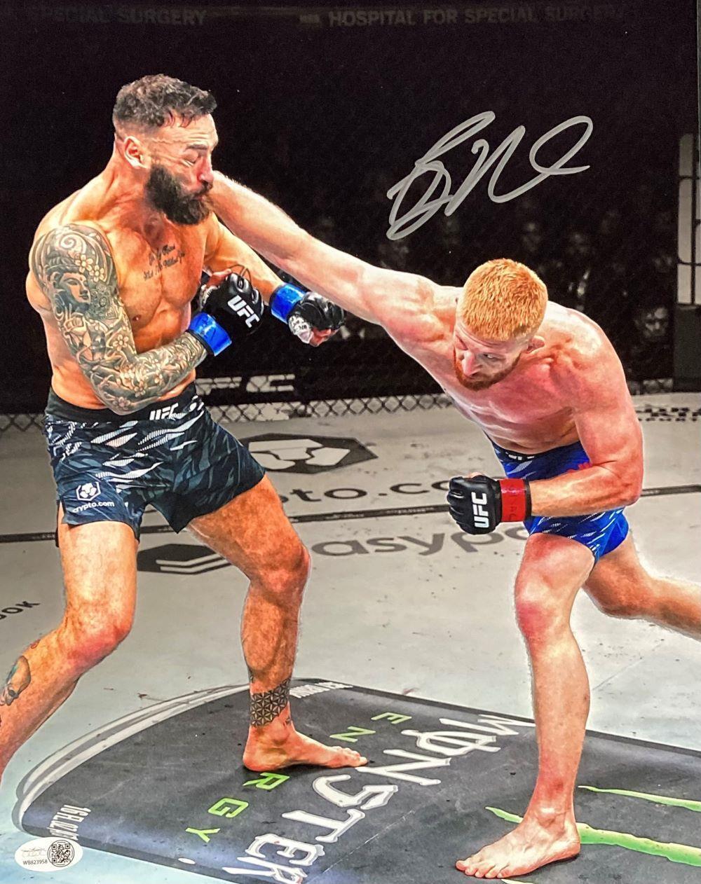 Bo Nickal, in blue shorts, lands a punch during an MMA fight against a bearded, tattooed opponent in black shorts. This 11x14 photo is signed and authenticated by JSA ITP. Brand: Sports Integrity.