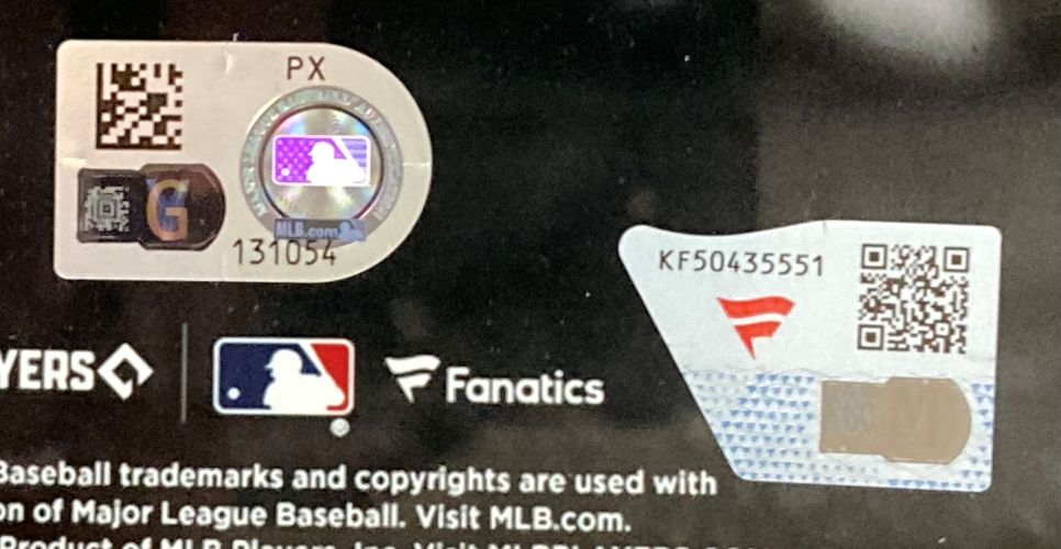 Close-up of authentication and QR code stickers on the Sports Integrity Adley Rutschman Signed Framed 11x14 Baltimore Orioles Photo Fanatics packaging, featuring holographic MLB and Fanatics labels above the printed MLB logo and copyright text.