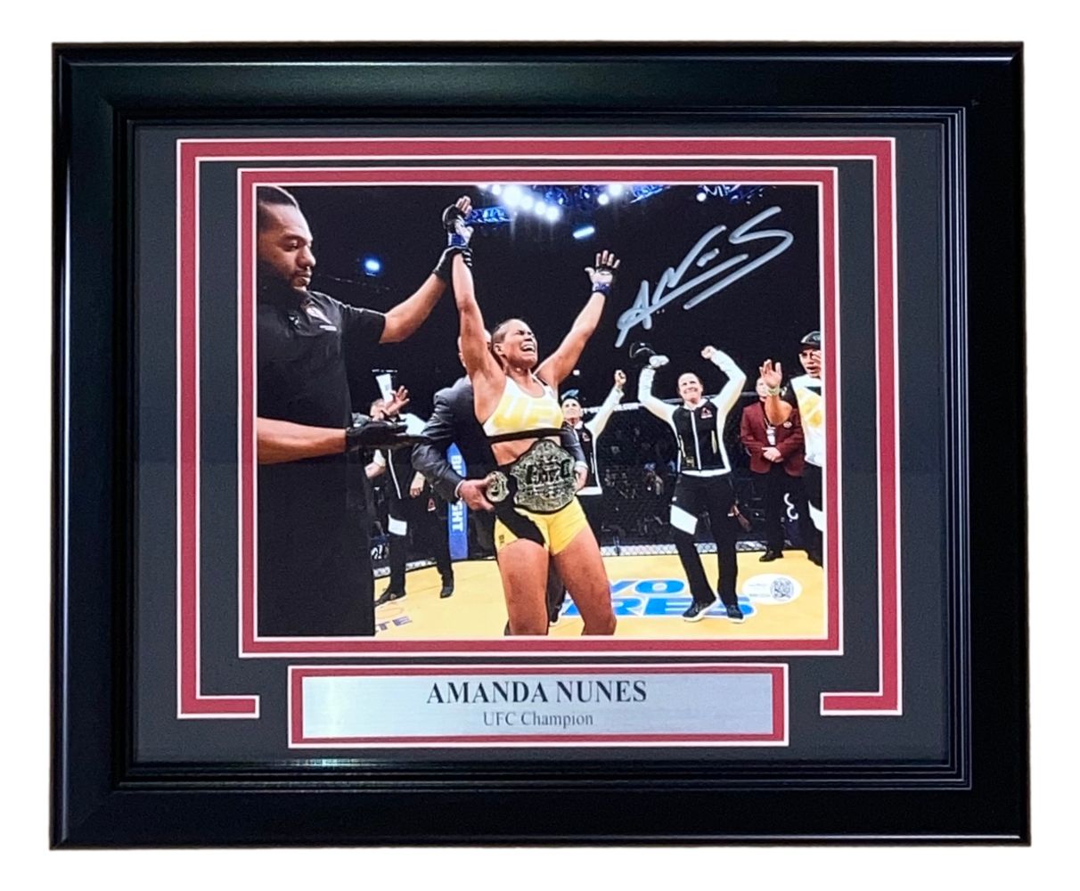 This Sports Integrity Amanda Nunes Signed Framed 8x10 UFC Championship Photo features her celebrating with a belt and includes a JSA QR Hologram, plus a silver plaque inscribed “UFC Champion” below the image.