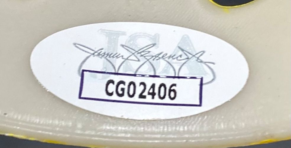 A white oval sticker labeled CG02406 with a faint blue logo and black signature is attached to the Ari Lehman Signed Jason Vorhees Yellow Costume Mask from Sports Integrity.