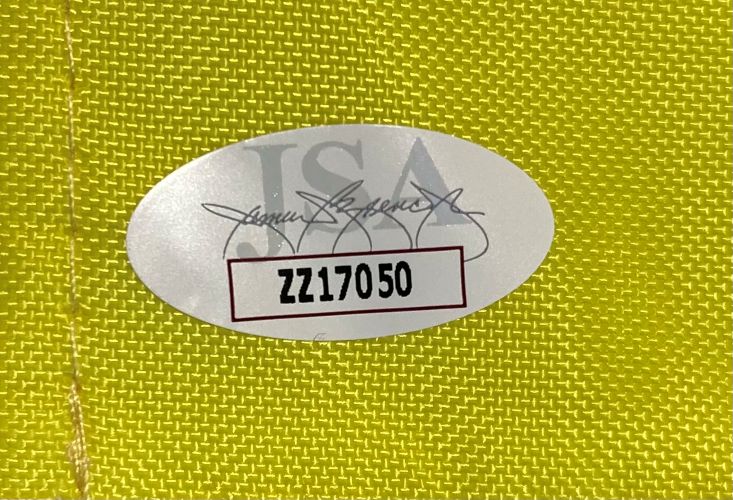 A white oval sticker with code ZZ17050 in bold black letters is on a yellow Arnold Palmer Invitational golf flag from Sports Integrity, featuring faint grey text and a stylized signature in the background.