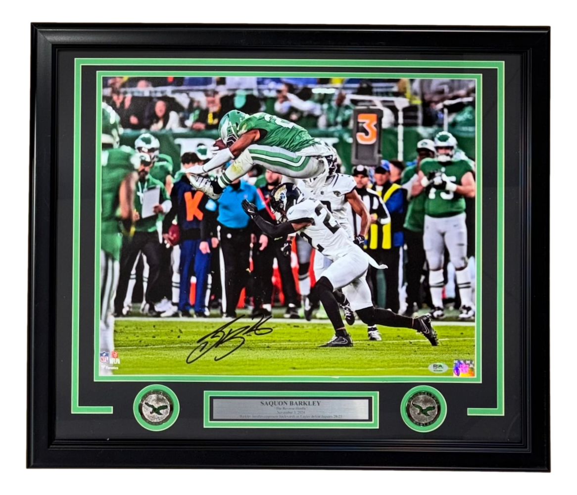 The Sports Integrity Saquon Barkley Signed Framed 16x20 Eagles Reverse Hurdle Photo (PSA/DNA) features Barkley leaping over an opponent, displayed with two coins and a nameplate below the autographed image.