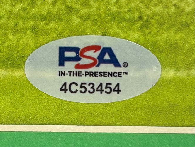 Close-up of a PSA/DNA authentication sticker (code 4C53454) on a Saquon Barkley Signed Framed 16x20 Eagles Reverse Hurdle Photo by Sports Integrity, shown against a green and yellow background.