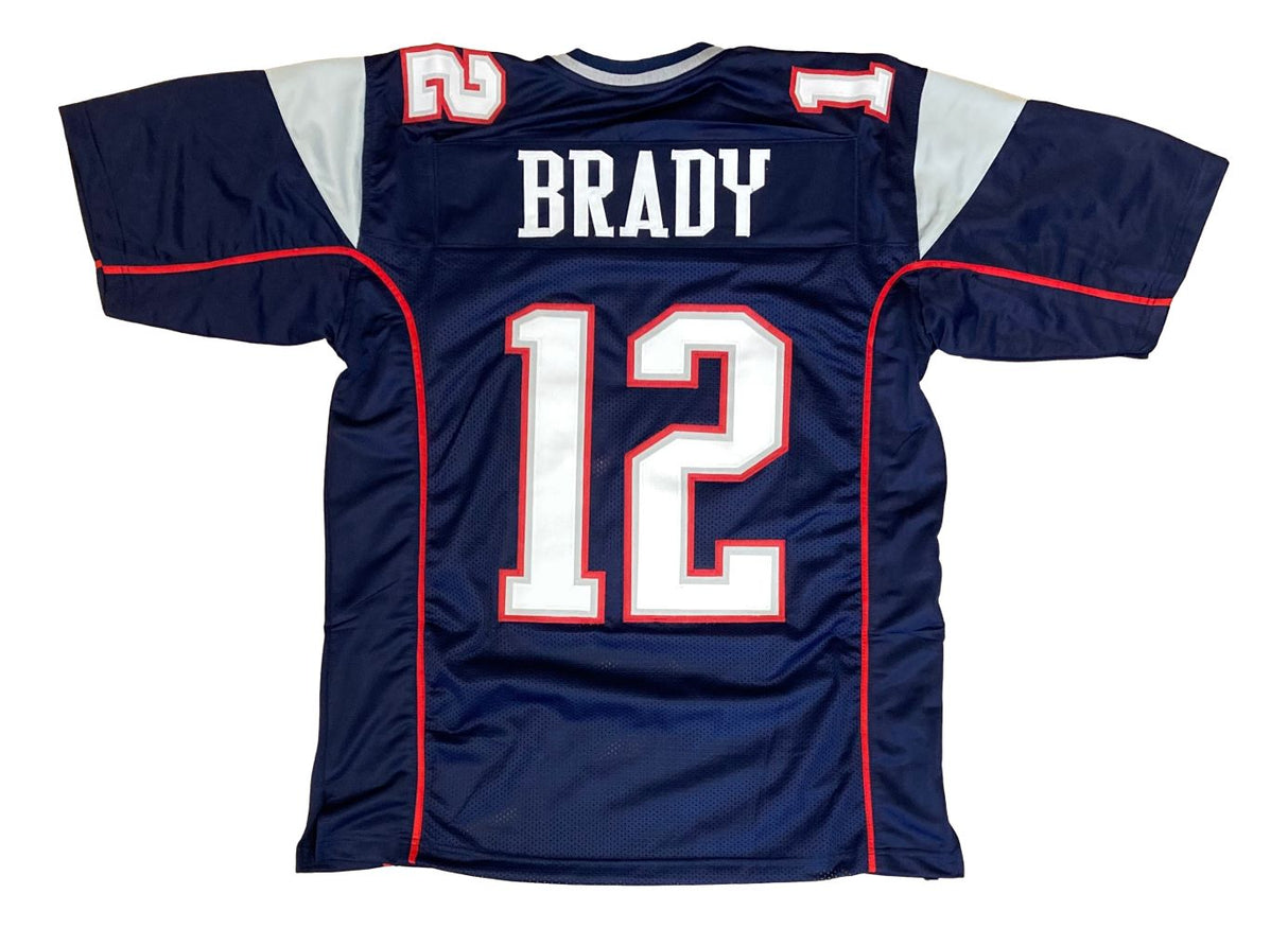 The Sports Integrity Tom Brady New England Blue Football Jersey features BRADY and the number 12 in white and red on the back, with white shoulder panels and red accents.