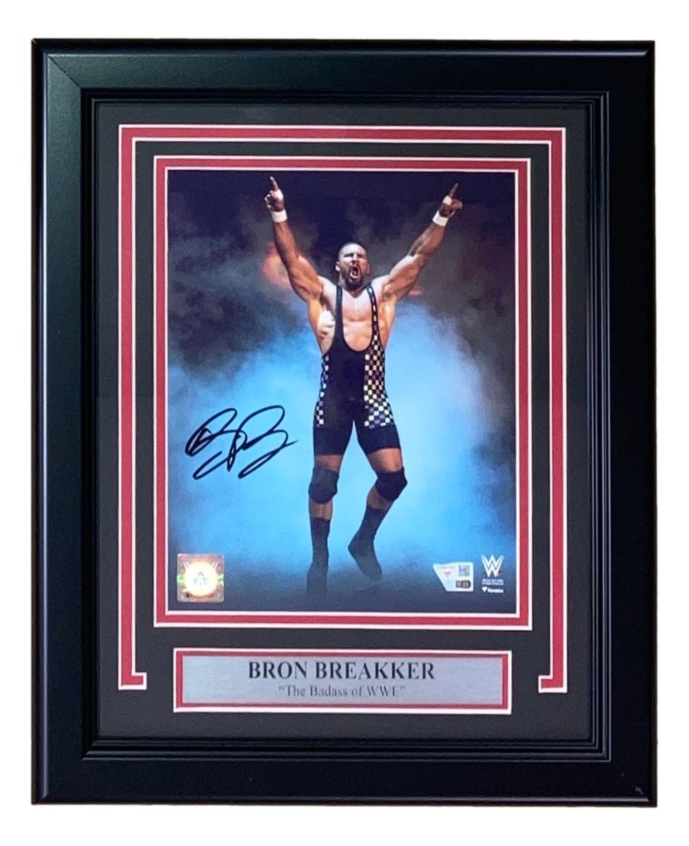 A signed and framed 8x10 WWE photo of wrestler Bron Breakker in a black checkered singlet, arms raised, from Sports Integrity. Features authentication logos and a plaque reading “Bron Breakker The Badass of WWE.”.