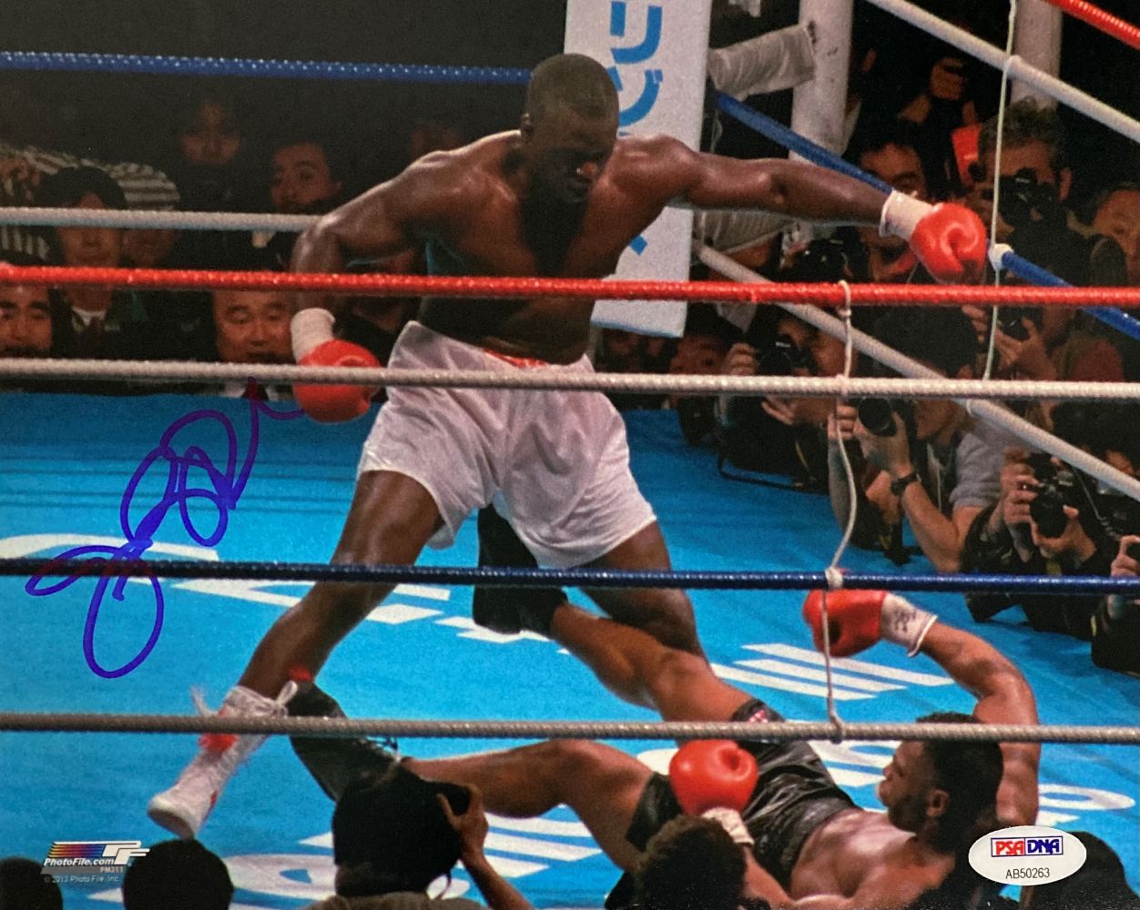 The Sports Integrity Buster Douglas Signed 8x10 Mike Tyson Knockout Photo (PSA/DNA) shows Douglas in white trunks standing over Tyson on the mat near the ropes, with his boxing glove signed in blue marker.