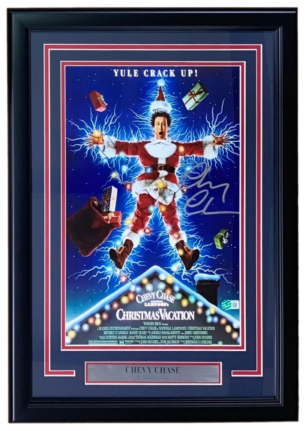 The Sports Integrity Chevy Chase Signed Framed 11x17 Lampoon’s Christmas Vacation Photo BAS features the iconic scene with a man shocked by Christmas lights, “YULE CRACK UP!” above, and a plaque with Chevy Chase’s name.