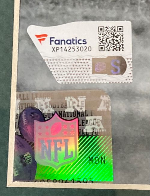 A close-up of authentication stickers on the Cooper DeJean Signed Framed 16x20 Eagles Hit vs D Henry Photo (Sports Integrity): one Fanatics sticker with QR code XP14253020, and a holographic NFL logo sticker labeled "MON.