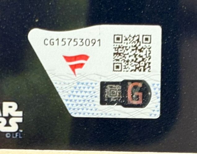 A close-up of a sticker with code “CG15753091,” red emblem, two QR codes, and a large G on a patterned background, seen on the Daisy Ridley Signed Framed 11x14 Star Wars Photo by Sports Integrity. Star Wars logo partially visible.