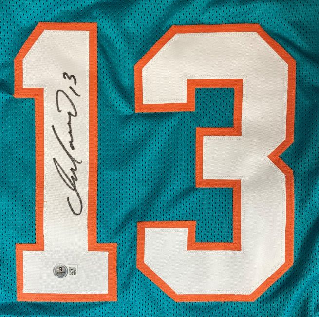 The Sports Integrity Dan Marino Miami Signed Teal Football Jersey BAS ITP features a large white and orange number 13 with Dan Marino’s signature in the number 1 and an authentication sticker below the autograph.