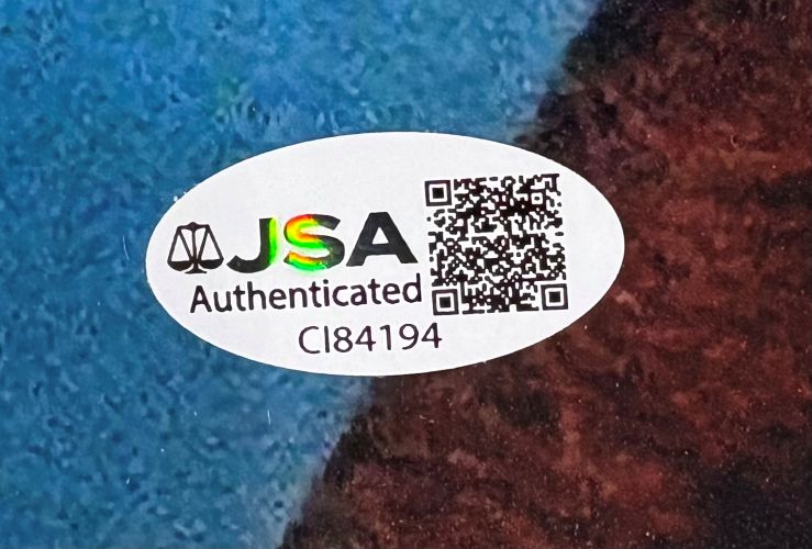 A white oval JSA Authenticated sticker with holographic logo, QR code, and ID CI84194 is affixed to the Matthew De Merritt Signed 11x14 ET Photo by Sports Integrity on a blue and brown background.