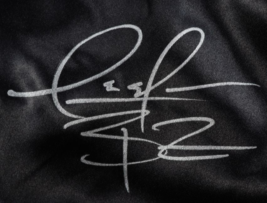 A stylized silver autograph with large, looping letters is signed on the black fabric of these Deontay Wilder custom boxing trunks from Sports Integrity. The signature appears abstract and is authenticated by BAS.