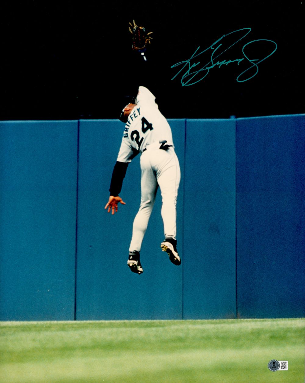 The Sports Integrity Ken Griffey Jr Signed 16x20 Seattle Mariners Wall Catch Photo (BAS) shows Griffey, jersey #24, leaping by a blue outfield wall with his arm outstretched to catch a ball. His name “Griffey” appears on his back.