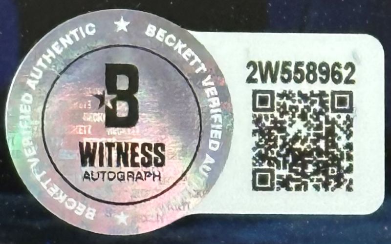 Close-up of a Beckett authentication sticker on the Allen Iverson Signed Framed 8x10 Philadelphia 76ers vs Kobe Bryant Photo by Sports Integrity, showing QR code, serial number 2W558962, and holographic B Witness Autograph Beckett Verified Authentic.