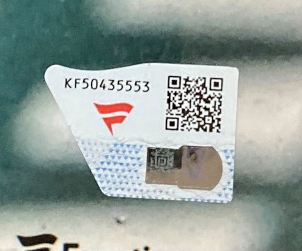 A close-up of a security sticker with a QR code, serial number KF50435553, a red F-like logo, and hologram on the patterned packaging of the Sports Integrity Jackson Holliday Signed Framed 16x20 Baltimore Orioles Photo.