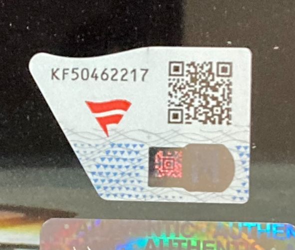 A security sticker with code KF50462217, QR code, red F, and hologram is affixed to a Jade Cargill Signed Framed 8x10 WWE Photo Fanatics by Sports Integrity on a reflective black surface.