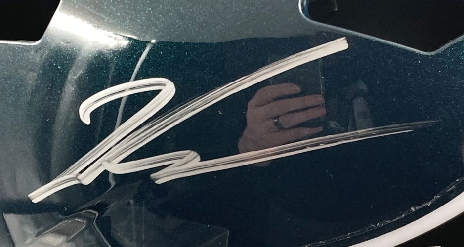 A close-up of a Jalen Carter Signed Eagles FS Replica Speed Helmet BAS with Super Bowl 59 LIX Case by Sports Integrity. The glossy dark green helmet displays a white autograph and faint phone reflection in its surface.