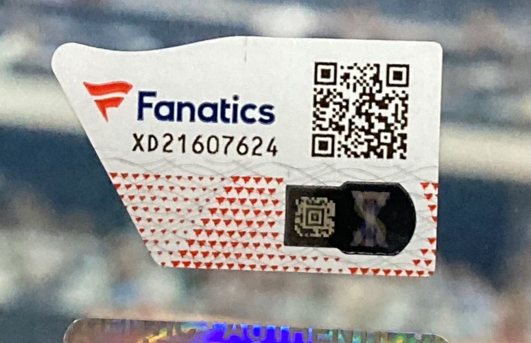 A close-up of a Fanatics authentication sticker with barcode, QR code, and serial XD21607624 on a Jey Uso Signed Framed 8x10 WWE Wrestlemania 41 Photo by Sports Integrity. The background is blurred.