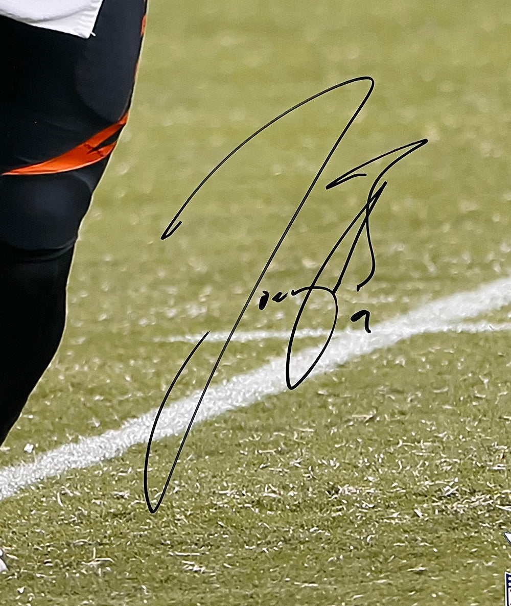 Close-up of a black ink autograph on a Joe Burrow Signed 16x20 Cincinnati Bengals Football Photo by Sports Integrity, showing the player's lower body in a dark uniform with a green field and white sideline in the background.