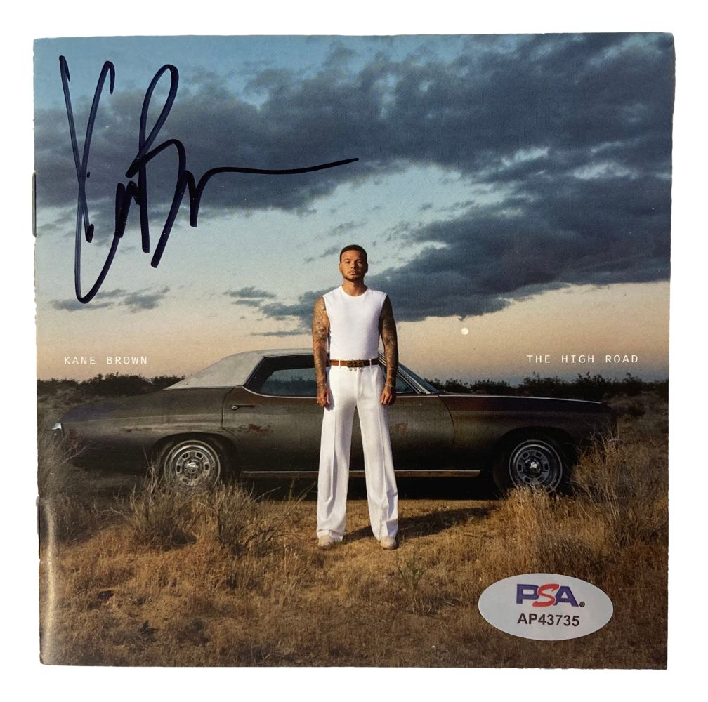 A Kane Brown Signed The High Road CD Booklet by Sports Integrity features his autograph in black marker and a PSA/DNA sticker “AP43735.” The cover shows Kane in white before a classic car at dusk, with cloudy skies and the text “Kane Brown The High Road.”.