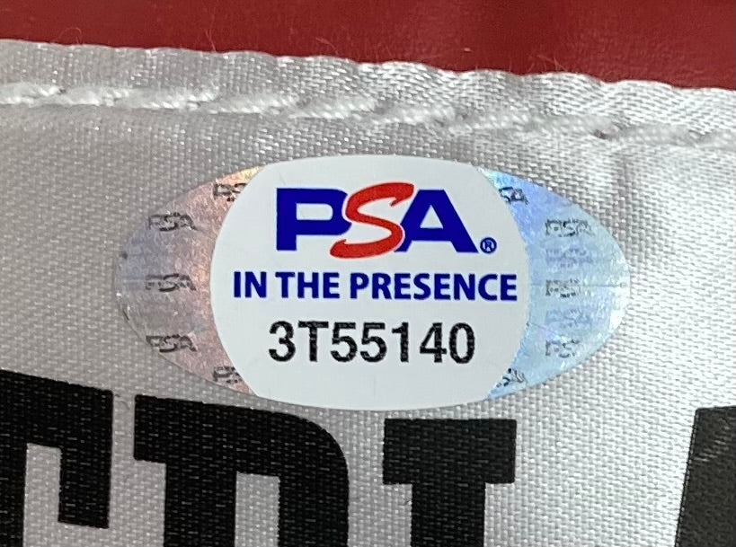 Close-up of a PSA authentication sticker reading "PSA IN THE PRESENCE 3T55140" on a white background, partially covering black print on a Dolph Lundgren Signed Everlast Boxing Glove I Must Break You Inscribed, by Sports Integrity.
