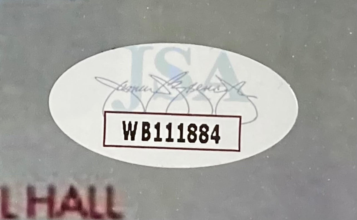 A white oval JSA authentication sticker with black code WB111884, JSA logo, and signature pattern is on the gray frame of the Molly Ringwald Signed Framed 11x17 Sixteen Candles Movie Poster Photo by Sports Integrity.
