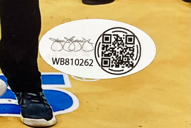 Close-up of a Sports Integrity Amanda Nunes Signed 8x10 UFC Championship Photo with a JSA QR hologram sticker, serial number WB810262, and signature shown on a yellow surface near a black shoe and blue/white graphic.