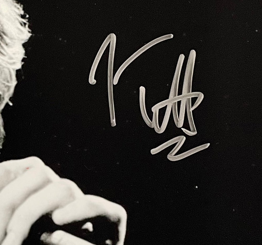 The Sports Integrity Joe Elliott Signed 11x14 Black and White Def Leppard Photo (JSA ITP) features a close-up of a hand holding a microphone, with Joe Elliott's large silver autograph across the image. The person's face is partially out of view.