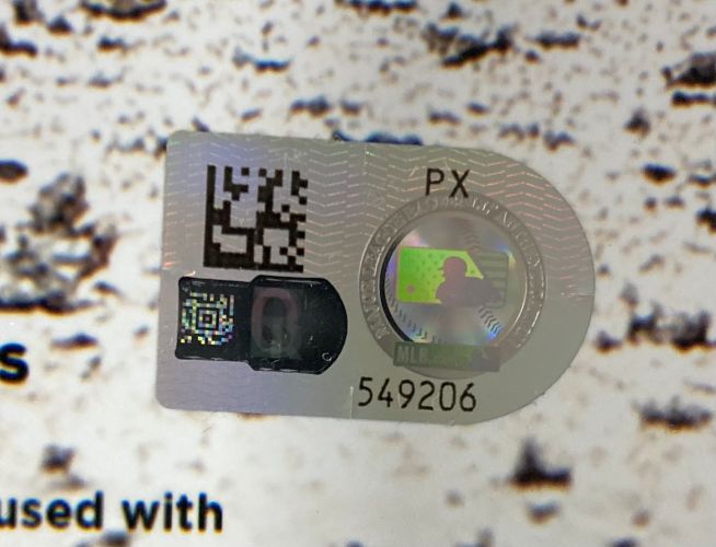 A close-up of a Sports Integrity holographic sticker with QR codes, "PX," and number 549206 on a Paul Skenes Signed 16x20 Pittsburgh Pirates Photo MLB Hologram, set against a textured background with partial printed text.