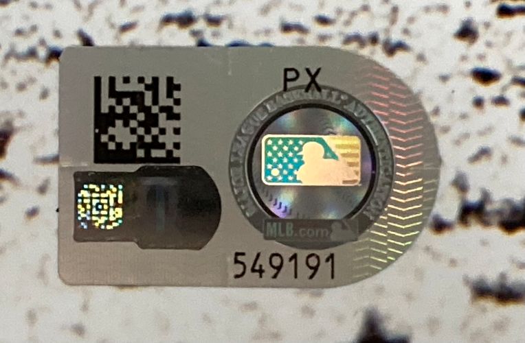 A close-up of the MLB authentication sticker with a QR code, hologram, and logo (number 549191) on the Sports Integrity Paul Skenes Signed Framed 16x20 Pittsburgh Pirates Black Jersey Photo. The background is speckled white and black.