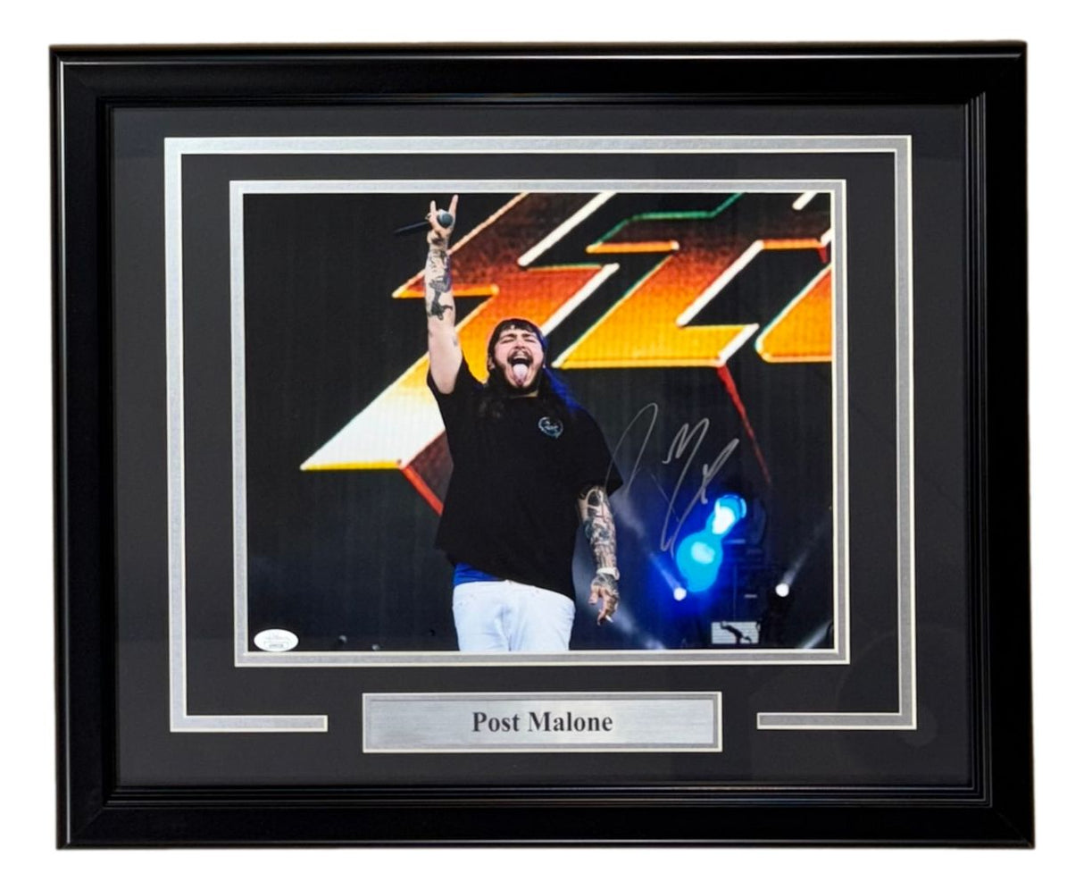 The Sports Integrity Post Malone Signed Framed 11x14 Photo (JSA) features Post Malone performing on stage, smiling with one arm raised, wearing a black shirt and white pants. A metallic nameplate beneath the image reads "Post Malone.