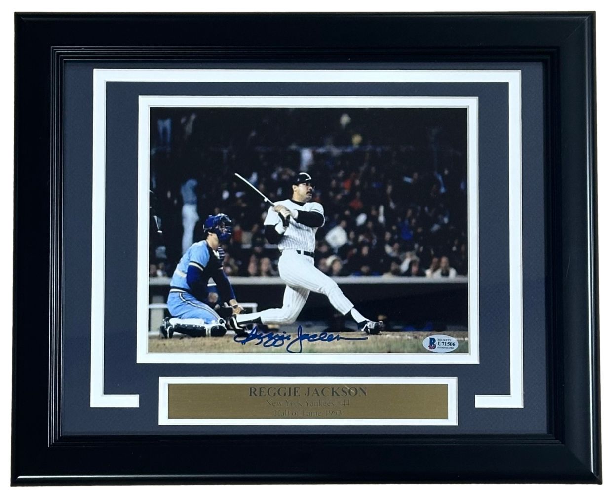 Sports Integrity Reggie Jackson Signed Framed 8x10 Photo shows him batting in the 1981 ALDS for the Yankees, with a catcher in blue gear behind. Includes a name plaque and BAS authentication.