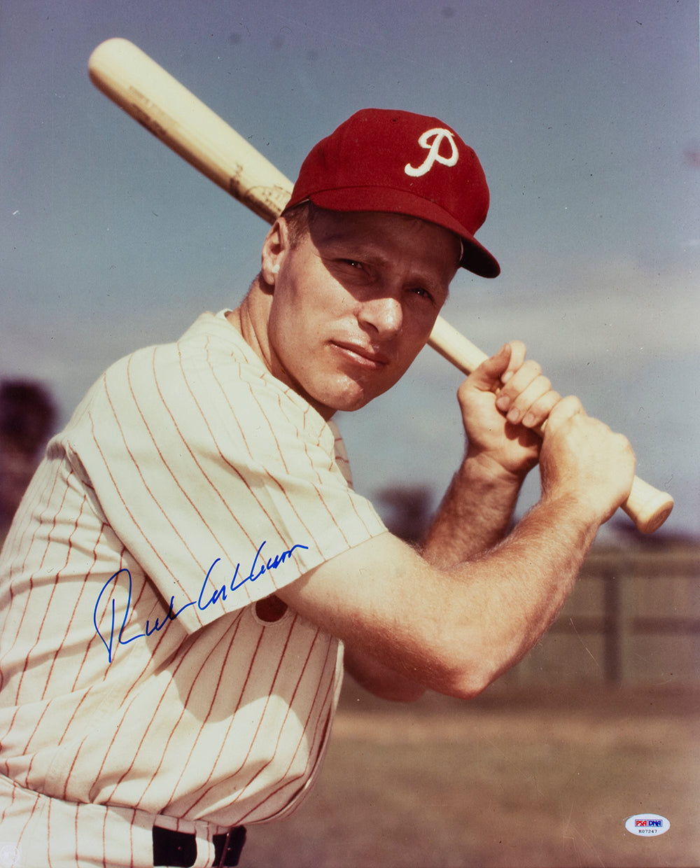 The Richie Ashburn Signed 16x20 Philadelphia Phillies Baseball Photo by Sports Integrity shows Ashburn in uniform and red cap, bat on shoulder, posing outdoors under a blue sky. Autographed and PSA/DNA authenticated.
