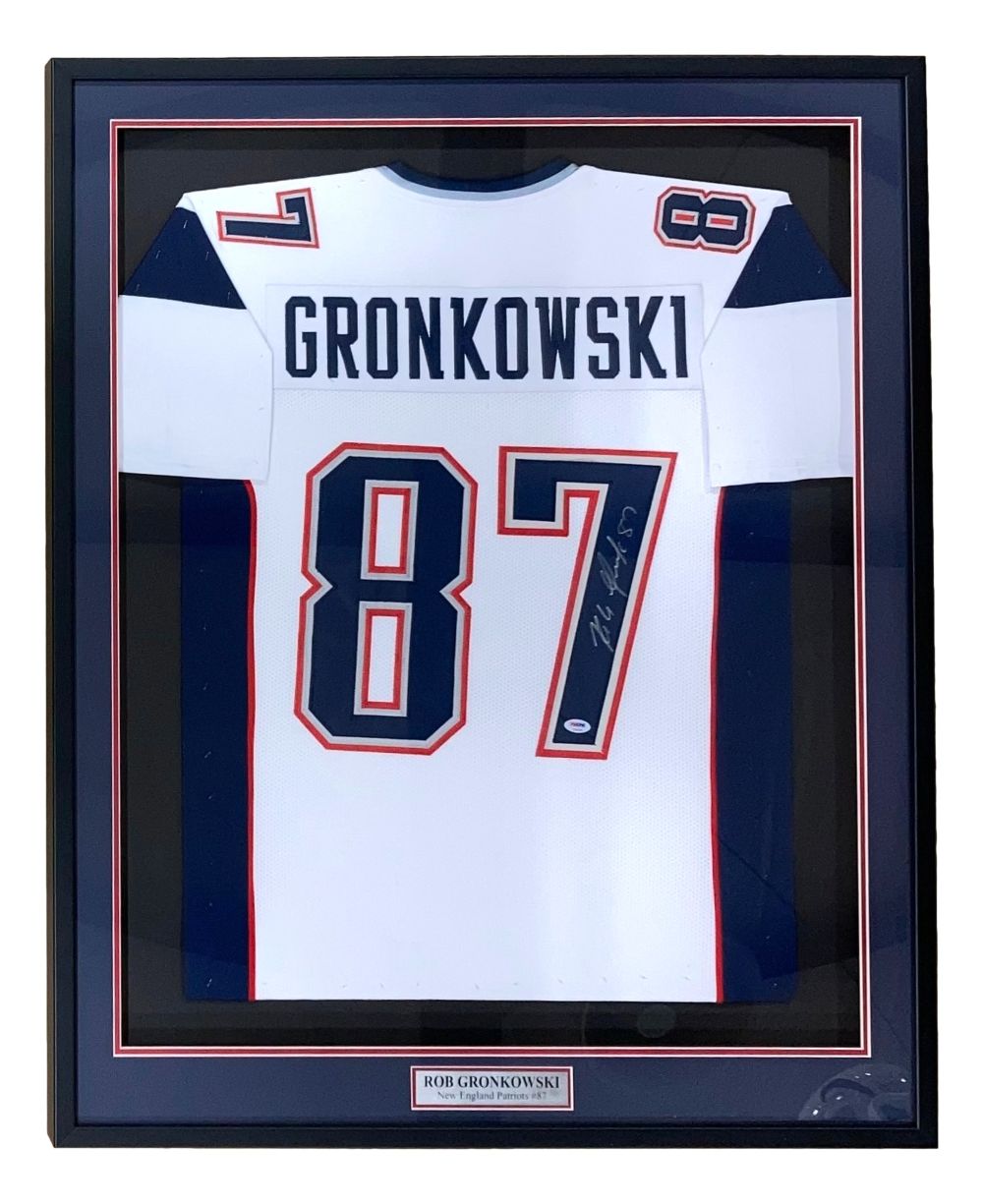 The Sports Integrity Rob Gronkowski New England signed framed white football jersey (#87) features his name, a PSA/DNA hologram, and is displayed in a black frame with a plaque at the bottom.