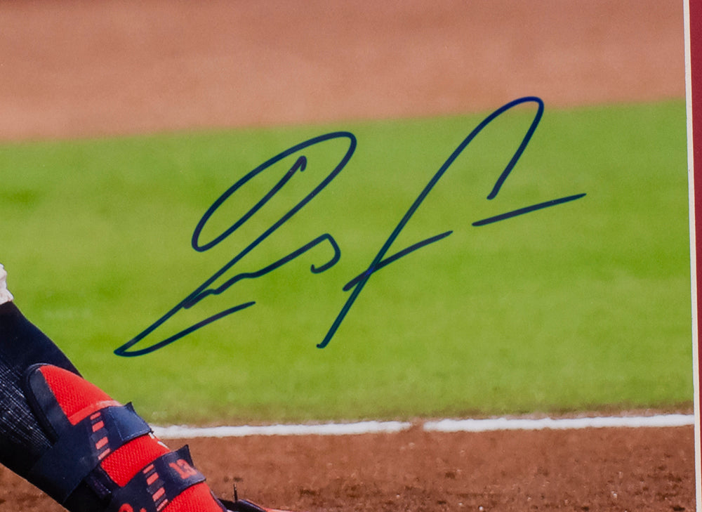 A close-up of a blue autograph on a Ronald Acuna Jr. Signed Framed 16x20 Atlanta Braves Baseball Photo by Sports Integrity, showing part of a player’s red and navy shoe, dirt ground, and green grass in the background.