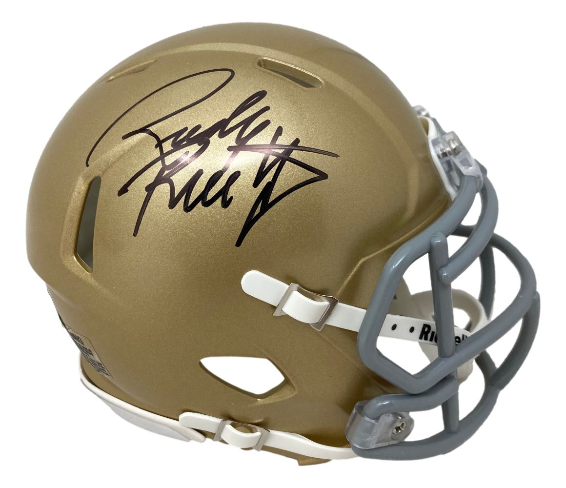 The Sports Integrity Rudy Ruettiger Signed Notre Dame Mini Speed Helmet BAS features a gold helmet with gray facemask, white chinstrap, and a prominent black autograph on the side.