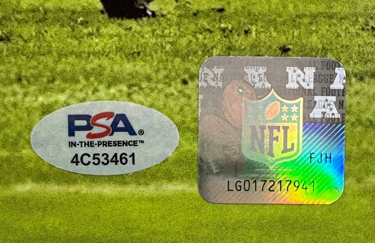 A Saquon Barkley Signed 16x20 Eagles Reverse Hurdle Color Photo by Sports Integrity features an oval PSA authentication sticker “4C53461” beside a square NFL hologram “LG017217941” on a green background with indistinct graphics.
