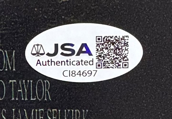 An oval white JSA Authenticated sticker with code CI84697 and a QR code is on a Sean Astin Signed 11x17 The Lord Of The Rings Fellowship Of The Ring Photo from Sports Integrity, placed on a dark textured surface with partial engraved text visible.