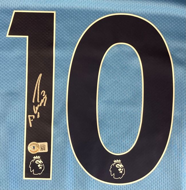 A close-up of a Sergio Aguero Signed Manchester City Puma Soccer Jersey by Sports Integrity, showing a large black number 10 outlined in white, the Premier League lion logo, Aguero's signature, and an authenticity sticker.