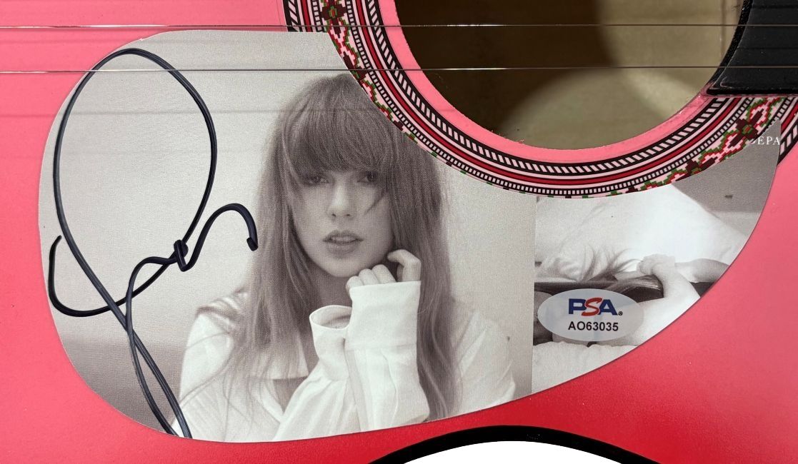 This Taylor Swift Signed 38" Tortured Poets Department Pink Acoustic Guitar from Sports Integrity features her black signature, a black-and-white photo of Taylor with long hair and bangs, and PSA authentication sticker AO63035.