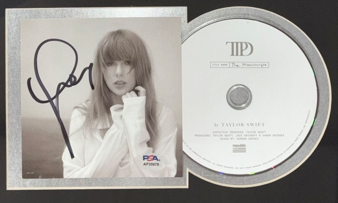 A Taylor Swift Signed Framed Insert with an 8x10 concert stadium photo, authenticated by PSA/DNA, from Sports Integrity is displayed alongside The Manuscript CD featuring the album title and artist’s name in simple black text.
