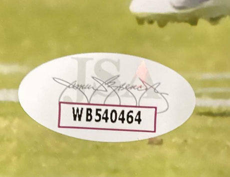 A Sports Integrity oval sticker with serial number WB540464, JSA letters, and faint signatures is on the grass next to a Jeremiah Trotter Jr Signed 8x10 Philadelphia Eagles Blocking Photo.