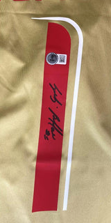 The Gianluigi Buffon Signed Italy Puma Gold Soccer Jersey by Sports Integrity features red and white stripes, a silver authentication sticker, QR code, and black autograph on gold fabric.