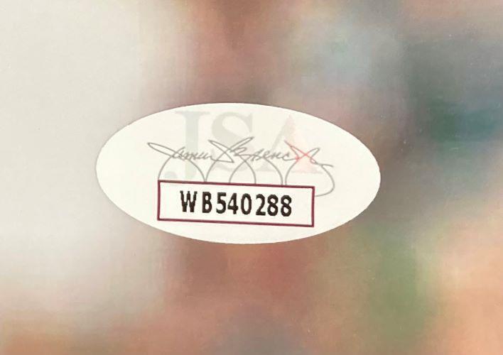 A white oval sticker with a faint printed signature, "JSA," and code WB540288 appears on this Brandon Graham Signed 8x10 Philadelphia Eagles Photo by Sports Integrity, set against a blurred, colorful background.