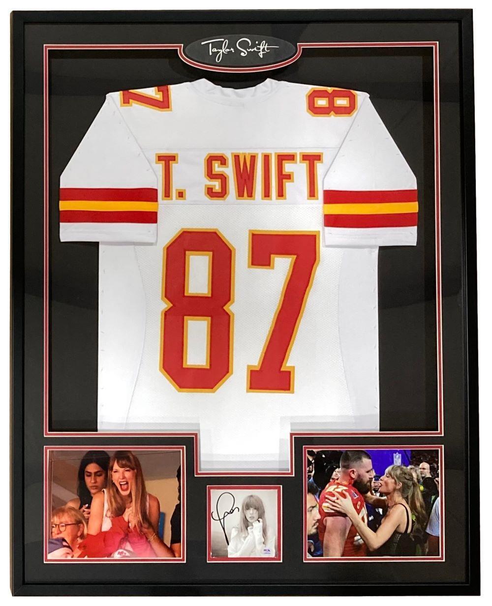 The Sports Integrity Taylor Swift Framed White Football Jersey w/ Signed Insert PSA/DNA features a Chiefs jersey labeled T. Swift 87, her autograph at the top, two photos of her cheering, and one photo with Travis Kelce.