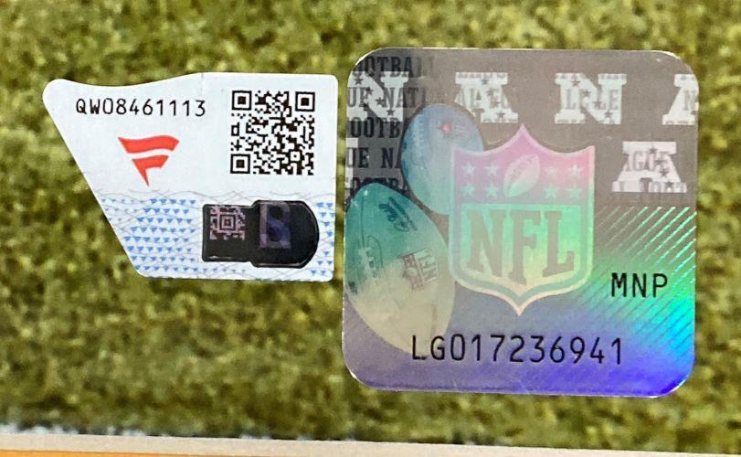 A close-up of two authentication stickers on the Justin Herbert Signed Framed 16x20 Los Angeles Chargers Running Photo Fanatics by Sports Integrity, one with a QR code and code, the other with a holographic NFL logo and serial number LG017236941.