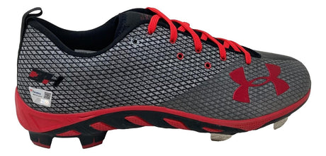 A pair of gray and black Bryce Harper signed Phillies Under Armour cleats by Sports Integrity, featuring a red sole, red laces, red Under Armour logo, and metal studs for traction.
