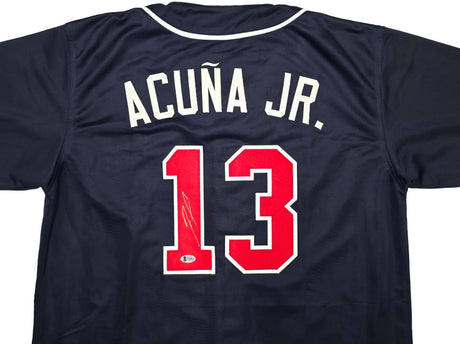 The Sports Integrity Ronald Acuna Jr Atlanta Navy Blue Baseball Jersey BAS features white "ACUÑA JR." lettering above a red and white number 13, signed in silver ink.